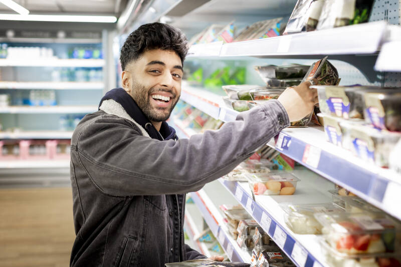 Smilimg student looking to camera while picking food item off the shelf